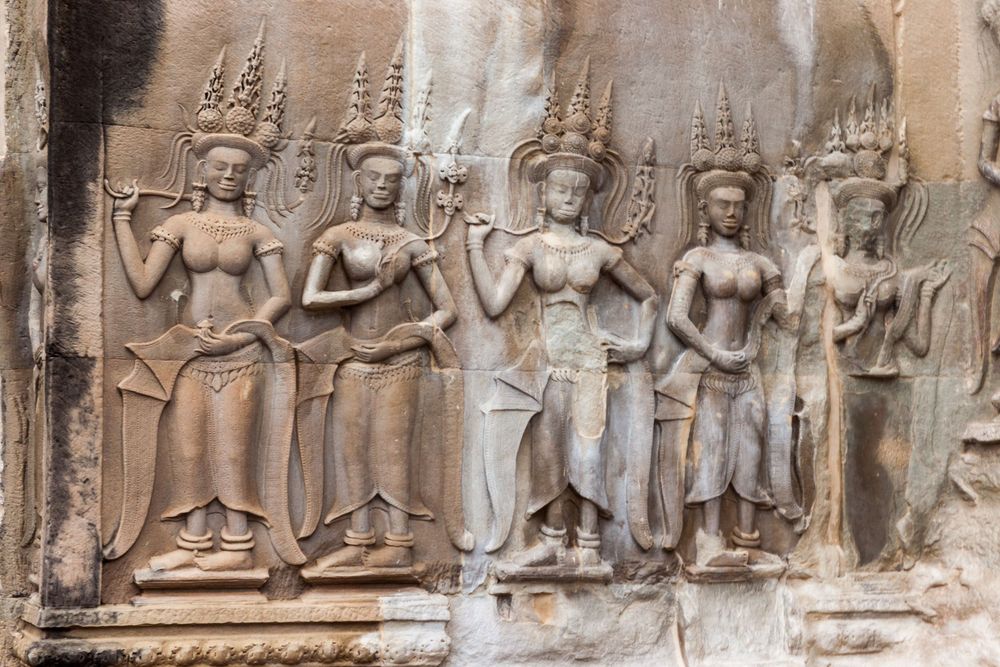 Ancient bas-relief stone carvings depicting detailed figures and scenes along a temple wall in Southeast Asia.