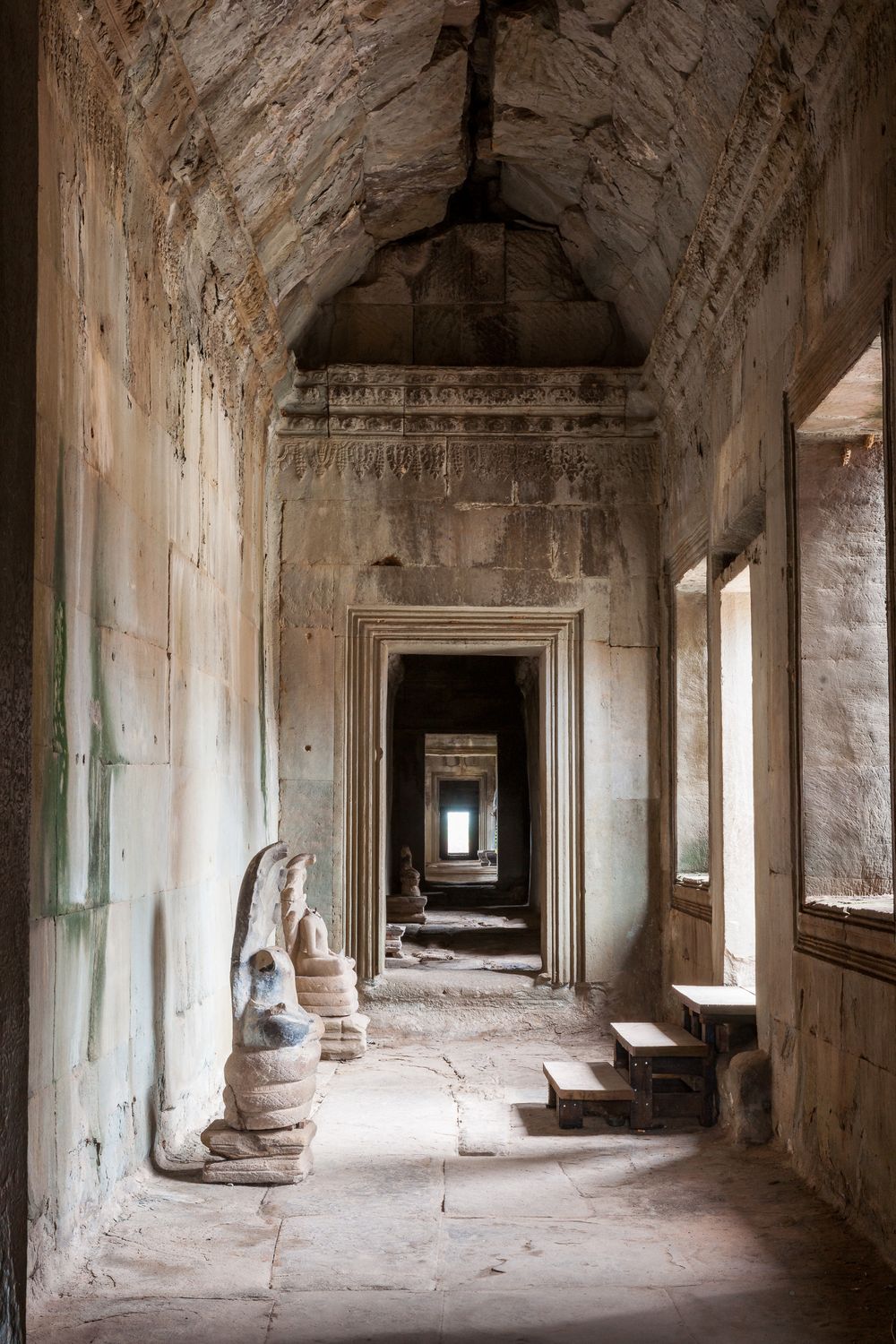 Panoramic view of ancient stone corridors with sunlit arches and columns in Angkor Wat temple complex.