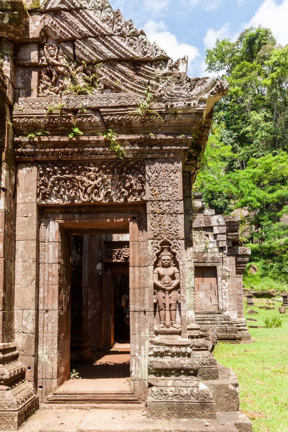 Ancient stone temple entrance with intricate carvings and statues at Wat Phu Champasak ruins in Laos.