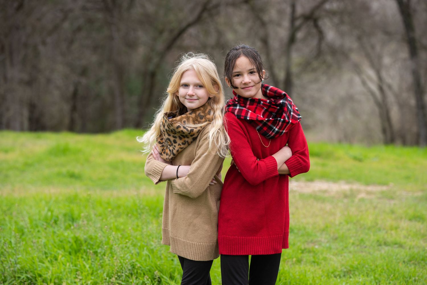 A couple in coordinating red and tan outfits stands together in a grassy outdoor setting in soft natural lighting.