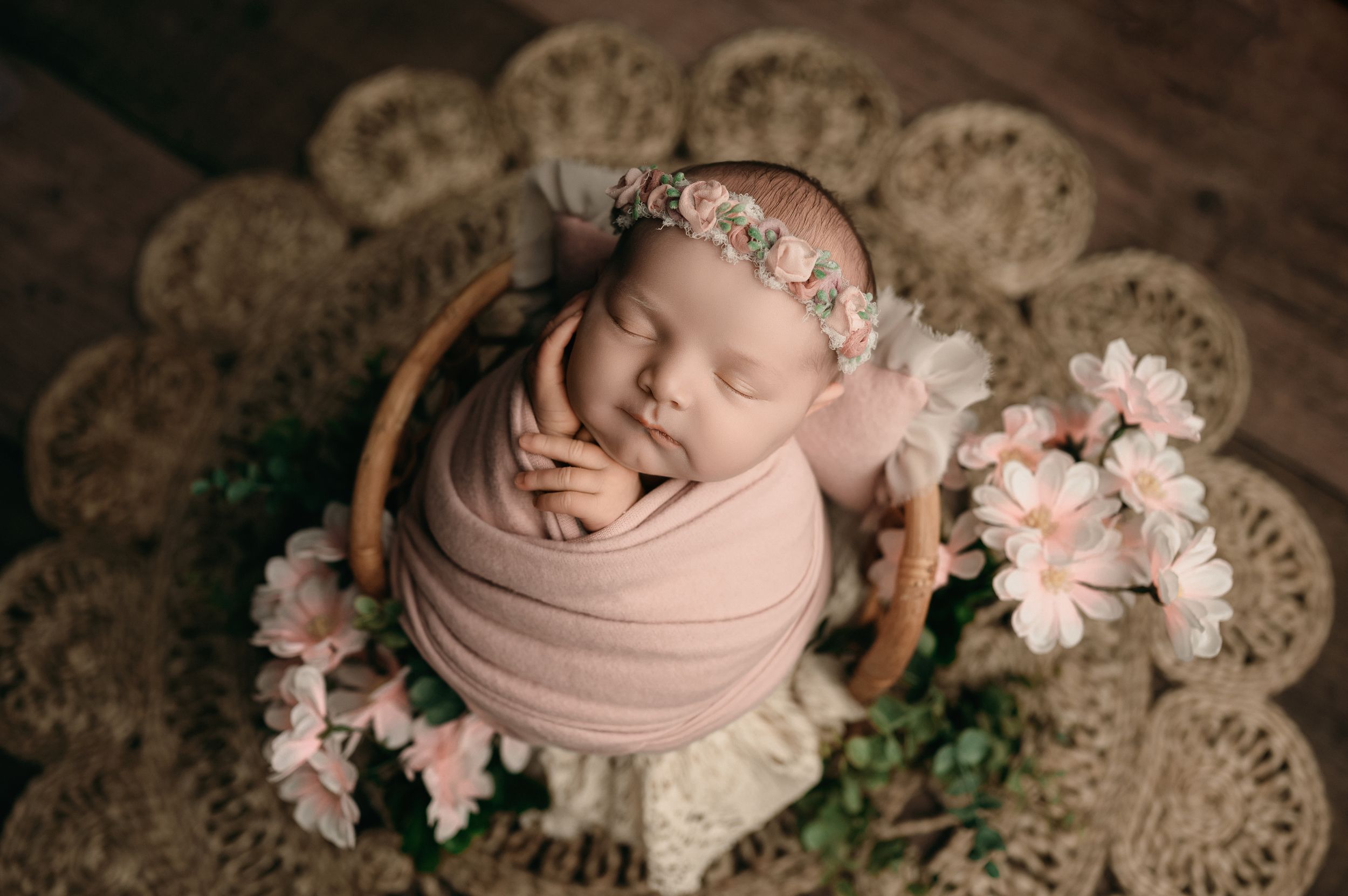 Rustic newborn photography setup with soft pink fabric, delicate lace doilies and floral accents in vintage styling.