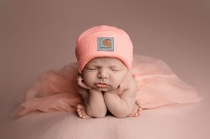 Six connected images of a newborn baby in pink wearing a knit hat while sleeping in various peaceful poses on pink fabric.