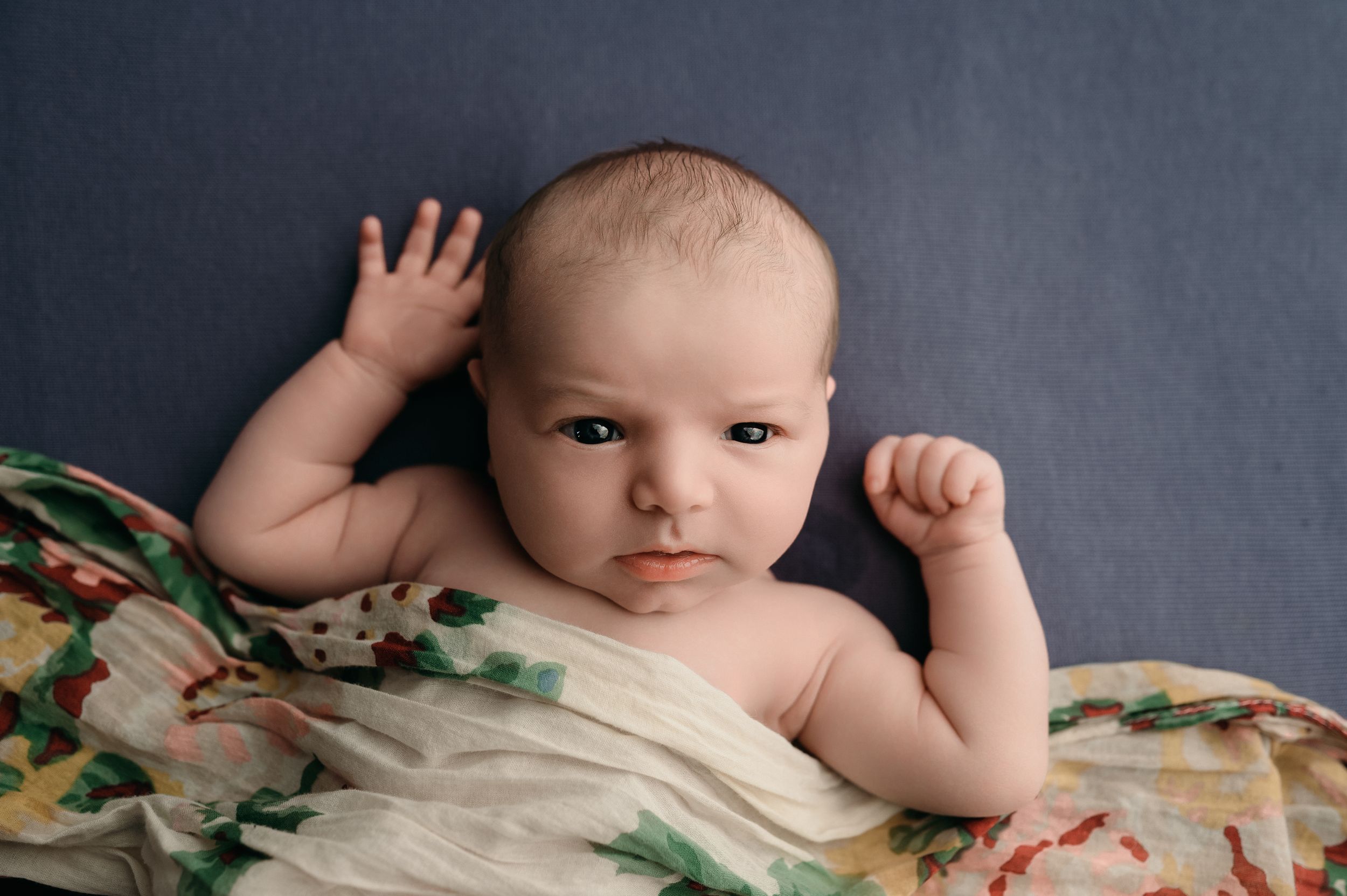 Professional newborn photography series showing a baby lying on soft textured blankets with floral accents in muted lighting.