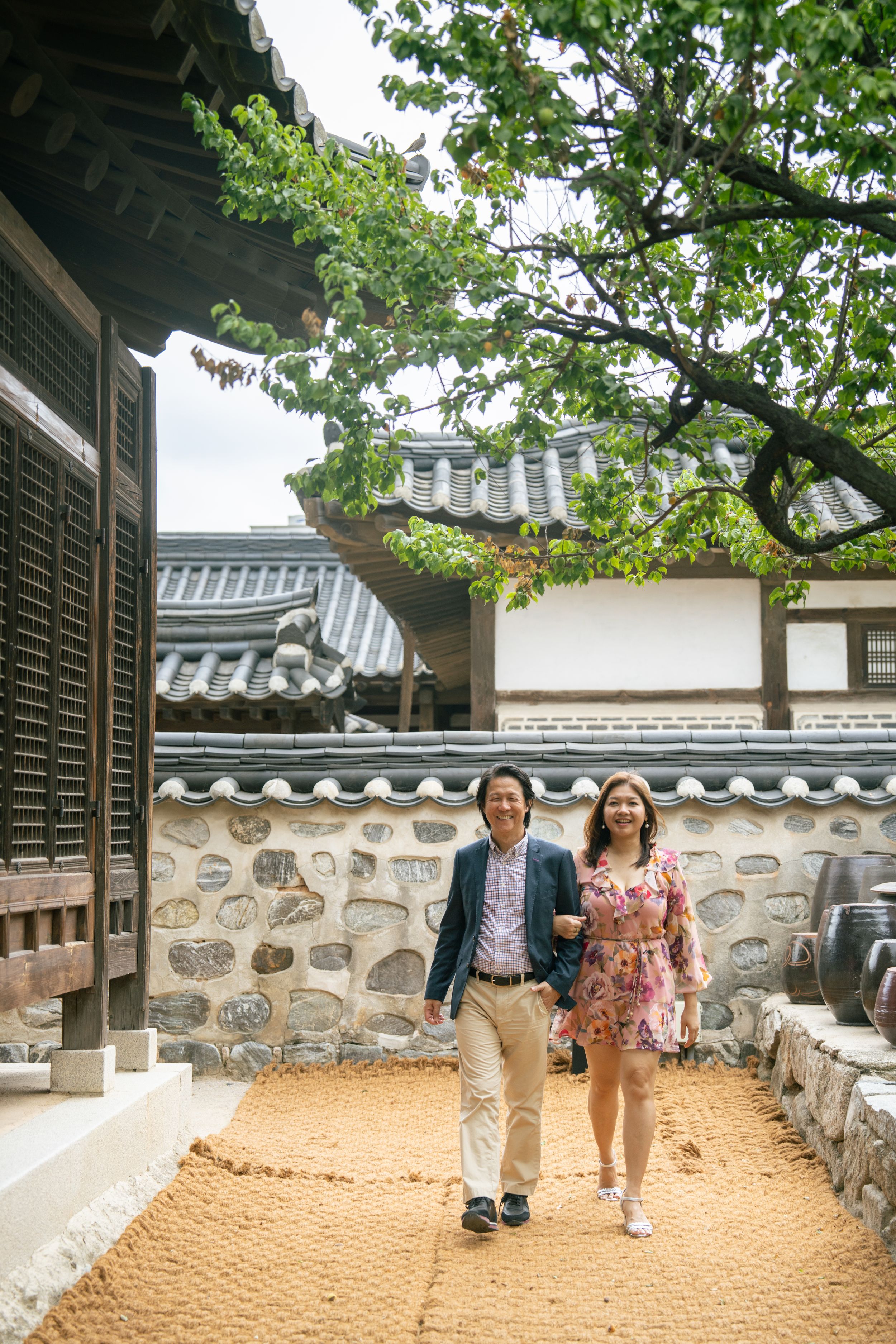 Sandy courtyard pathway between traditional stone walls and green trees in a Korean temple complex.
