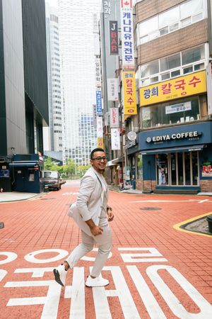 Person in white outfit posing on red brick street with Korean storefronts.