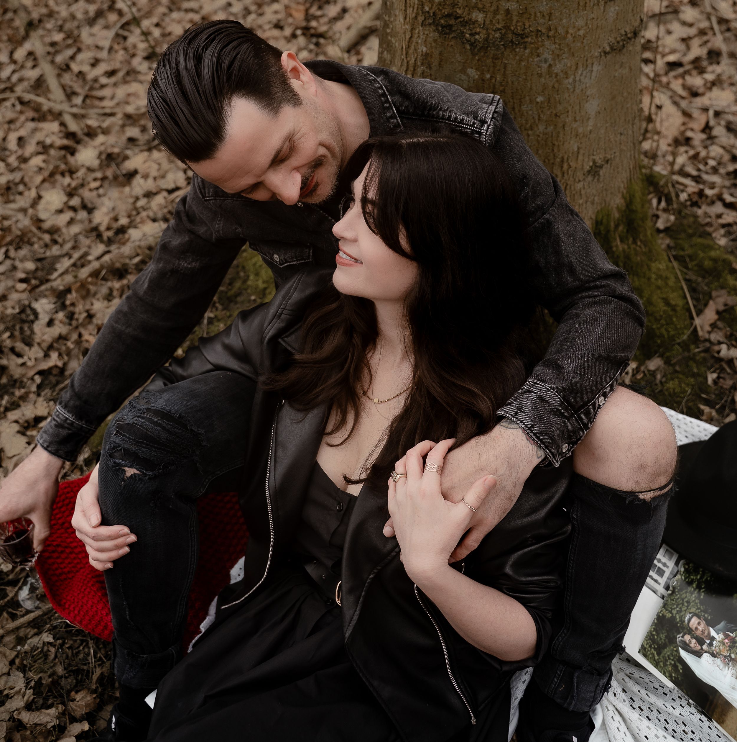 A couple in matching black leather jackets share an intimate moment while sitting outdoors in autumn.