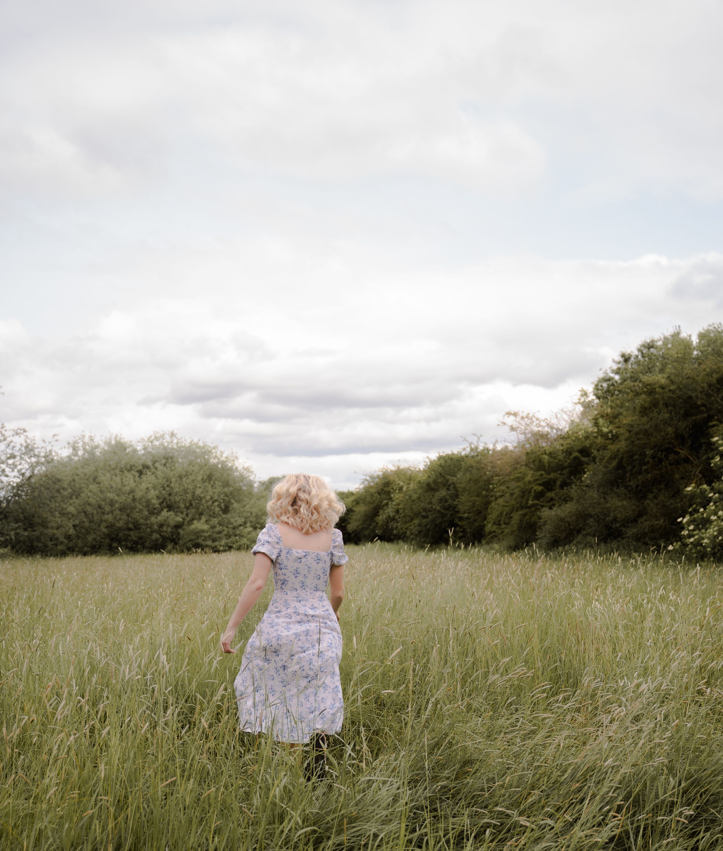 A sequence of photos shows a figure in a floral dress walking through a tall grass meadow on a cloudy day.