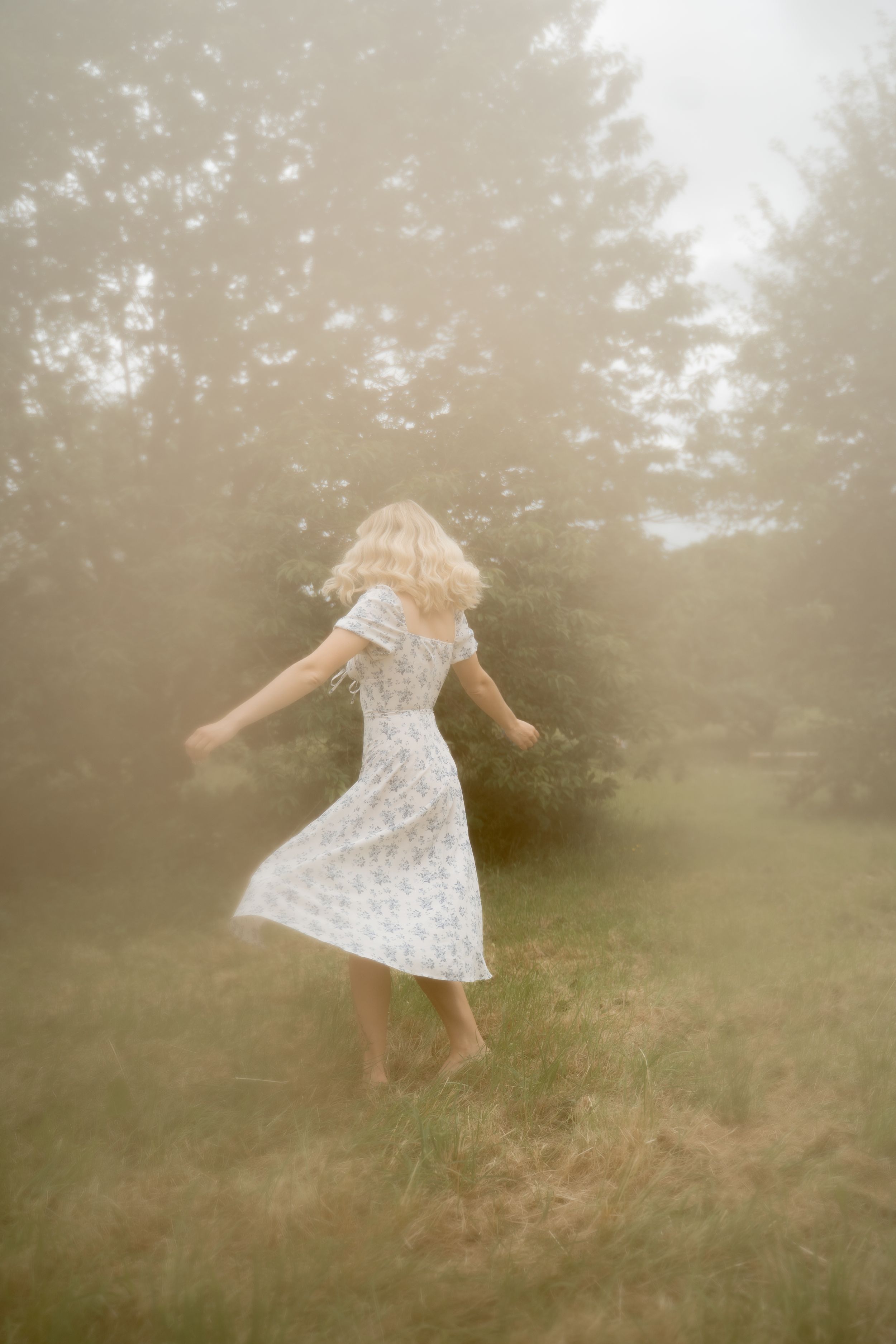 A dreamy sequence shows a person in a white floral dress twirling through a misty meadow on a foggy morning.