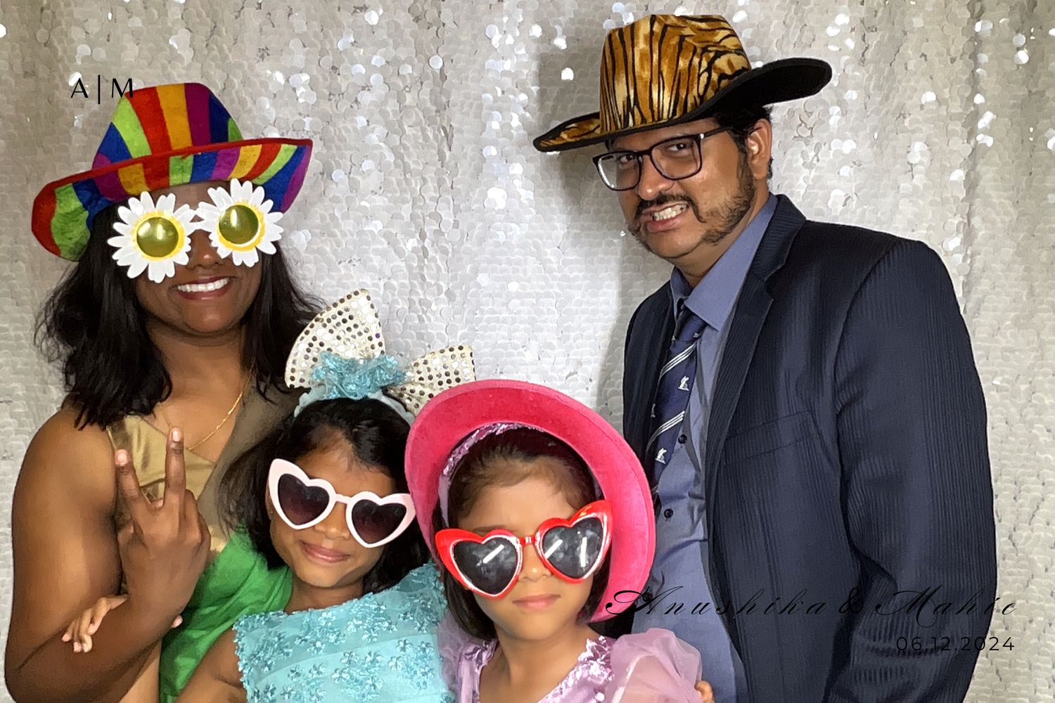 Group photo at a celebratory event with people wearing colorful sunglasses, hats and party accessories against a sparkly backdrop.