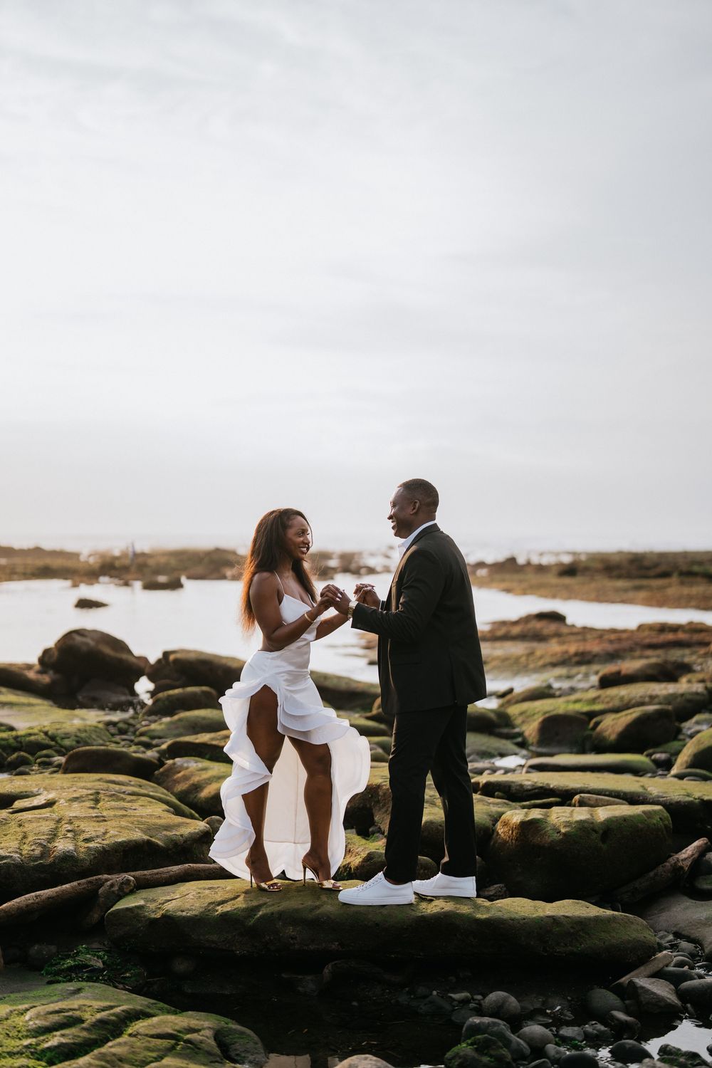 Couple in wedding attire sharing intimate moment on rocky coastal formation.