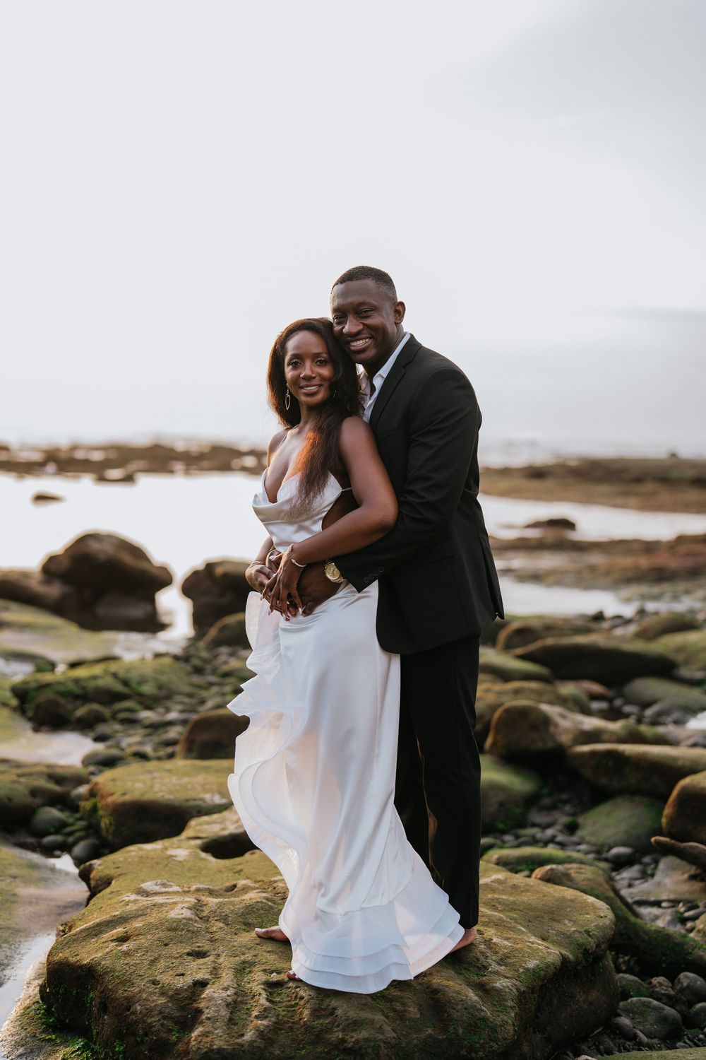 A loving embrace shared on rugged coastal rocks during a formal photoshoot.