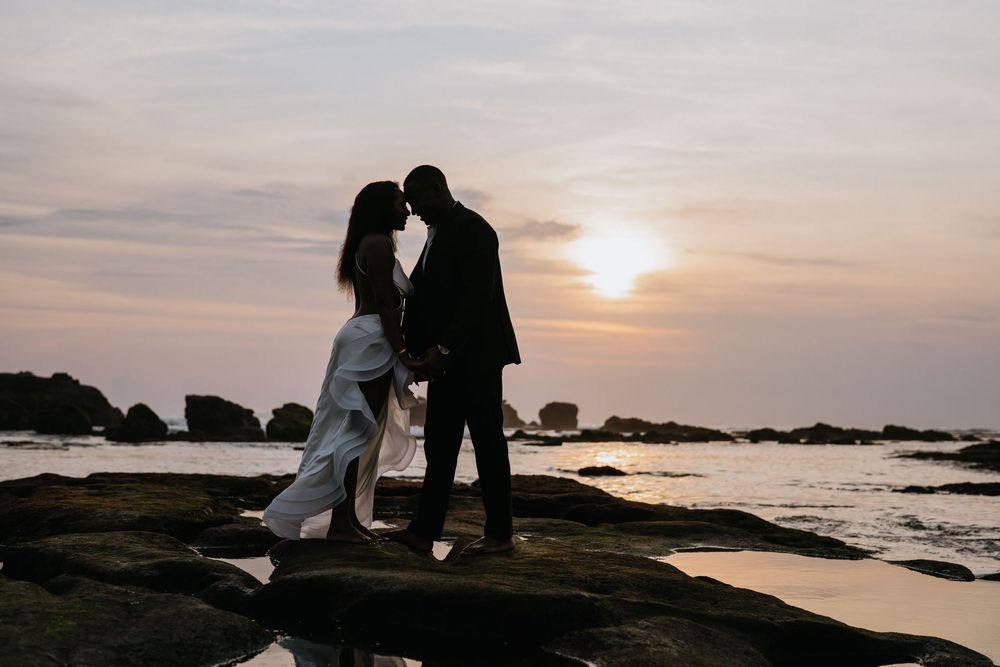 Silhouetted figures share an intimate moment on rocky cliffs during a golden sunset.