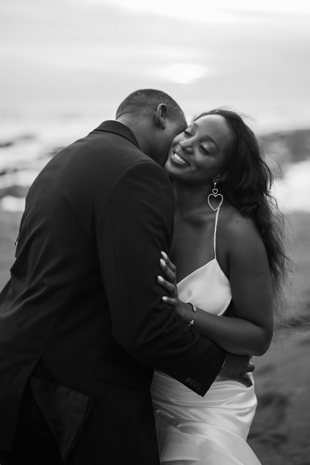 An intimate couple sharing a tender moment on a coastal beach at dusk.
