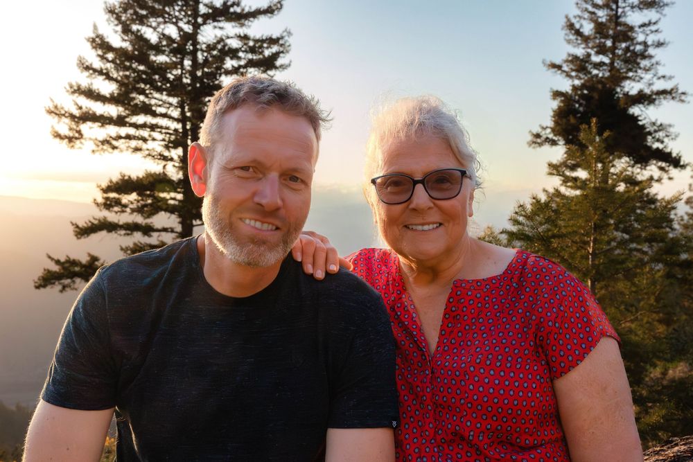 Family members pose together outdoors during golden hour with pine trees in background.