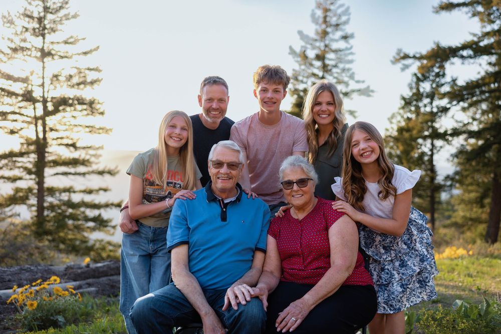 Multi-generational family poses together outdoors with evergreen trees and golden sunlight in the background.