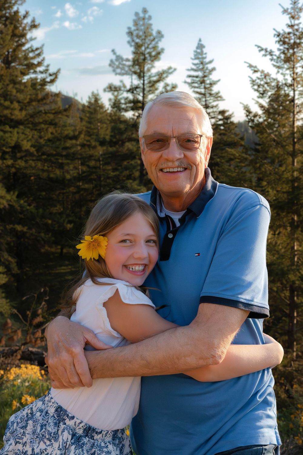 Heartwarming embrace between family members outdoors with pine trees and sunlight creating warm atmosphere.