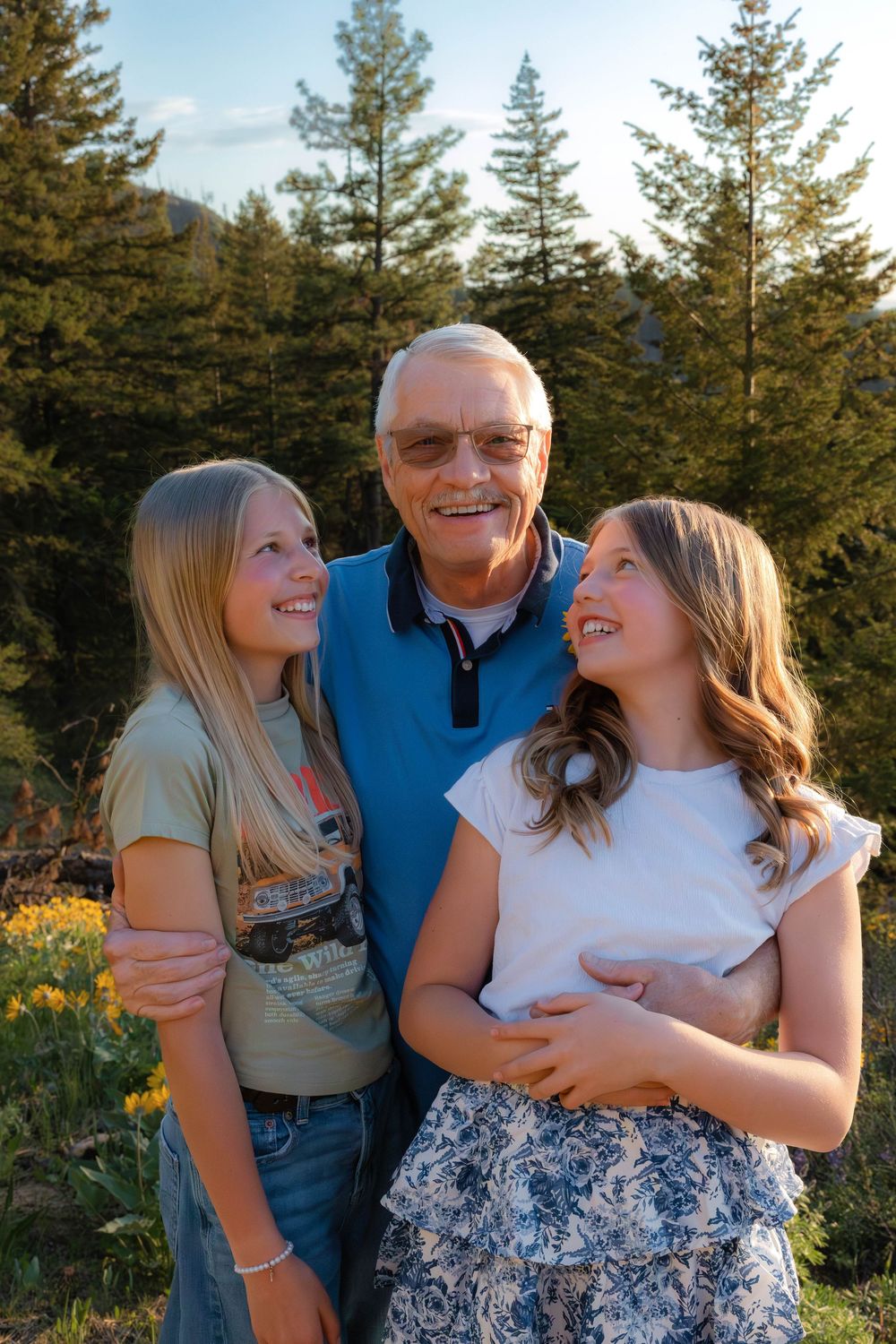Family members share joyful moment together outdoors with evergreen forest backdrop at sunset.