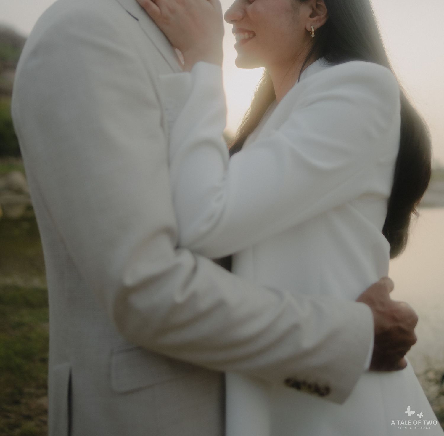 A romantic couple in matching white outfits share an intimate embrace outdoors in soft lighting.