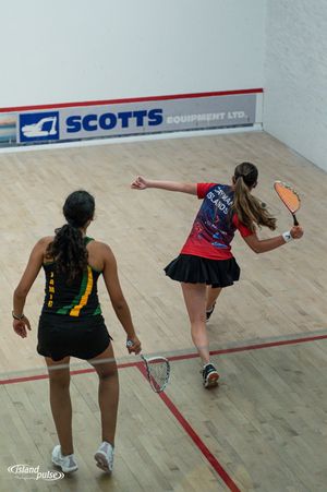 Two women playing squash on an indoor court with Scotts Equipment Ltd. signage visible in the background.