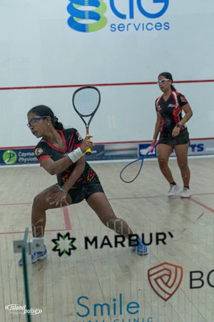 Two women playing squash on an indoor court with Marbury and Smile Clinic sponsor banners visible.