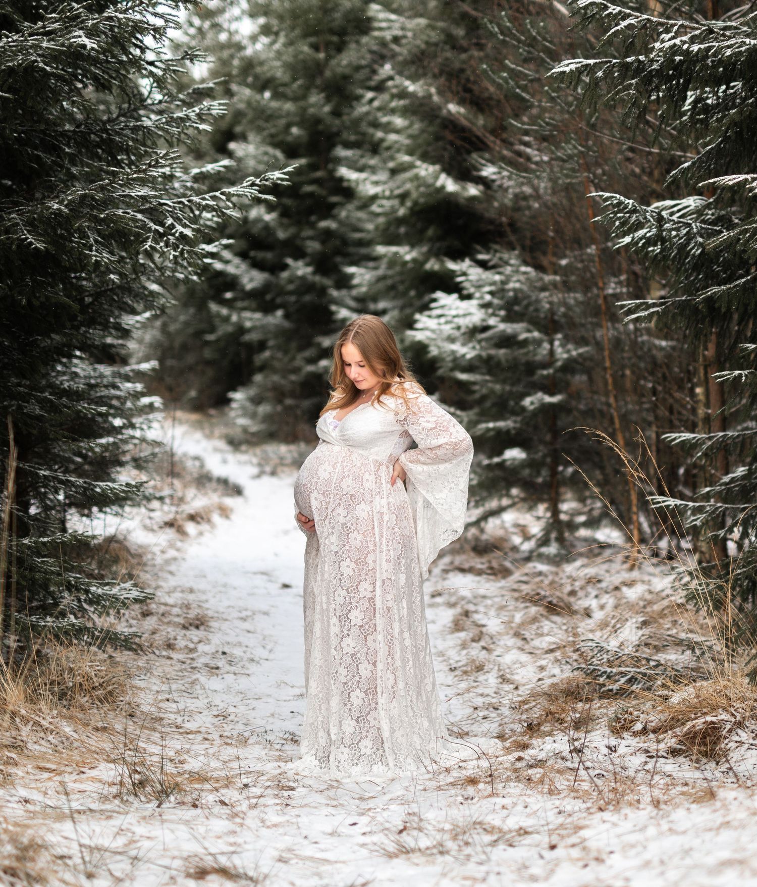 Gravid kvinna i en vit klänning i ett snöigt skogslandskap