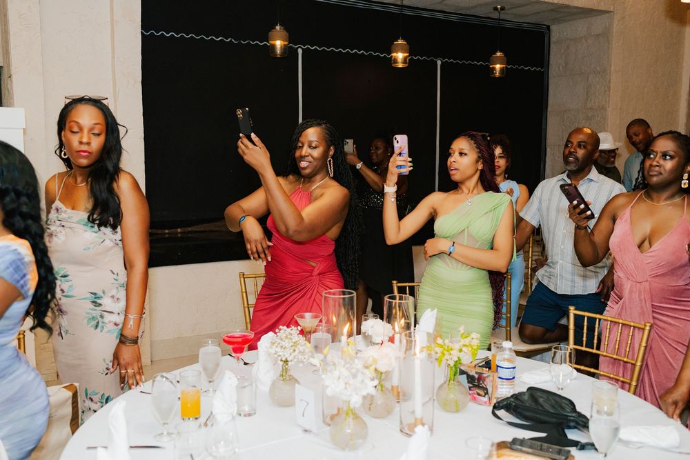 Wedding guests in colorful formal attire celebrate at a reception dinner table with drinks and candles.