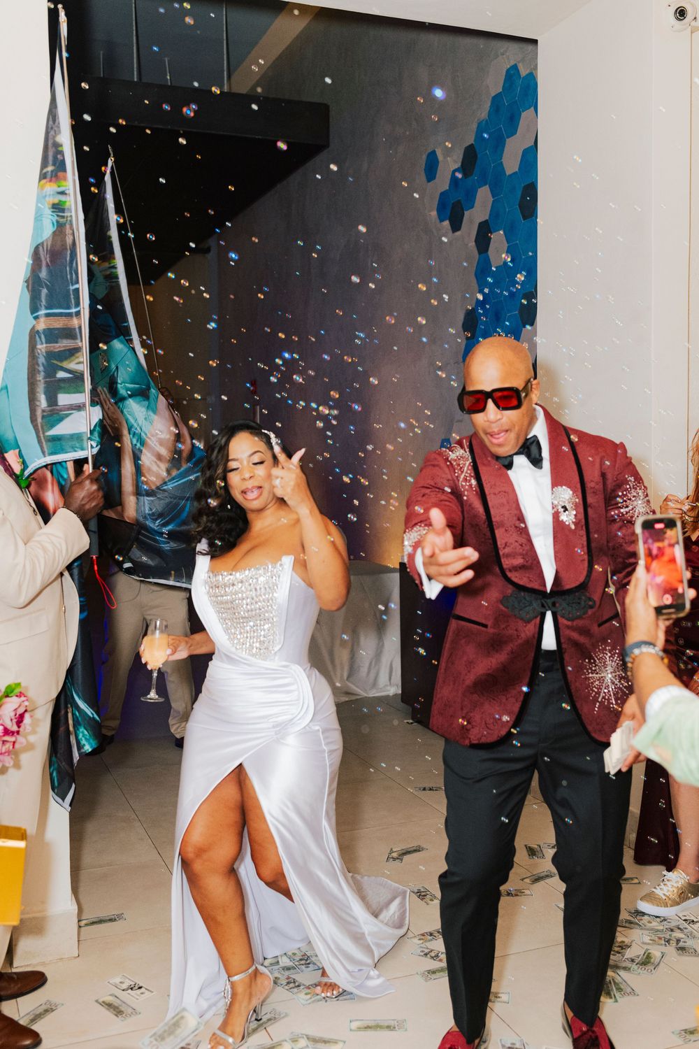 Newlyweds dance and celebrate at their wedding reception with confetti falling while wearing white gown and burgundy suit.