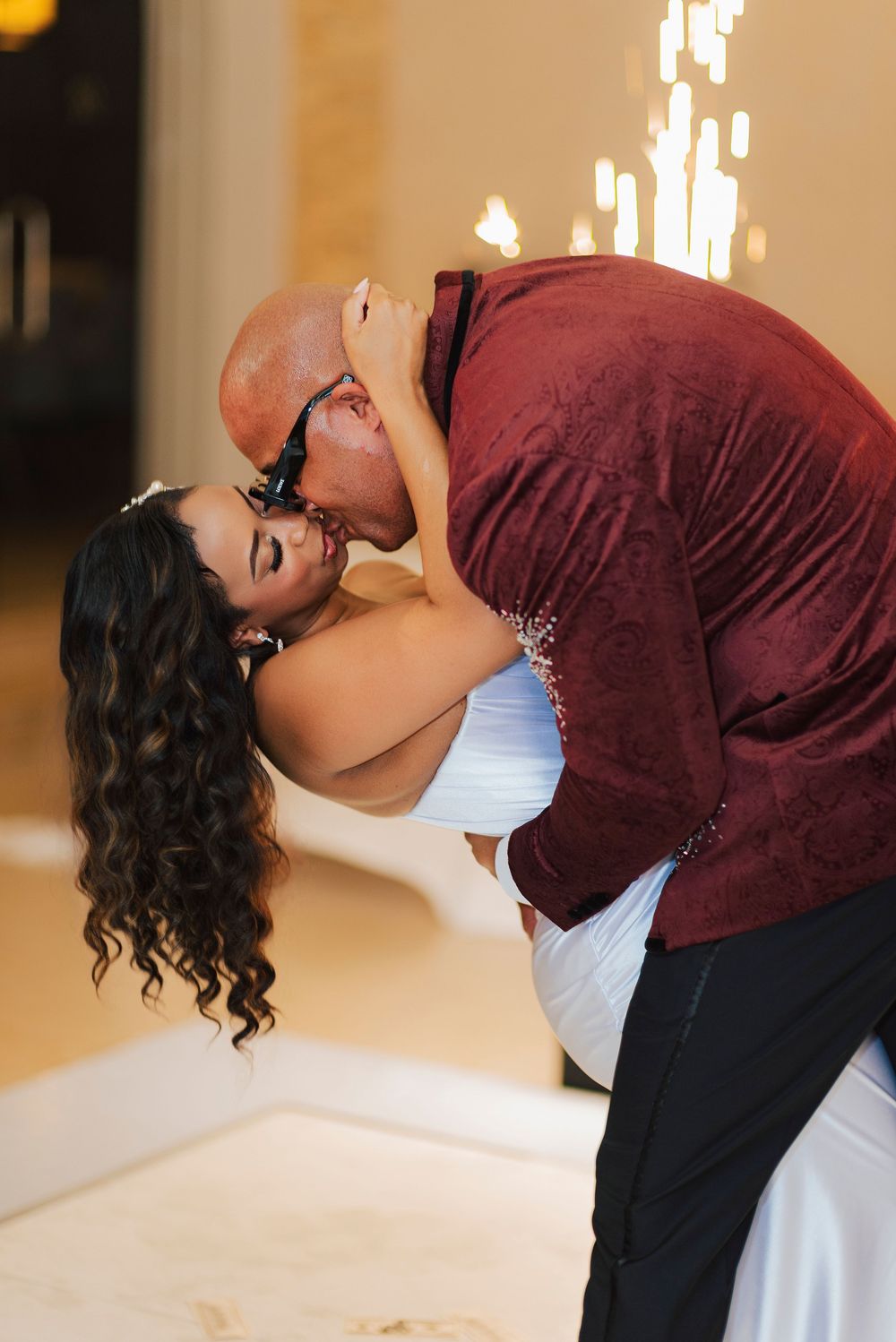 A couple performs a romantic dance dip move during what appears to be a wedding reception.