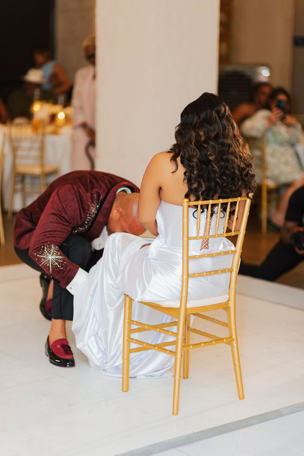 Dancers perform a dramatic dip sequence on a dance floor with gold chairs in the background.