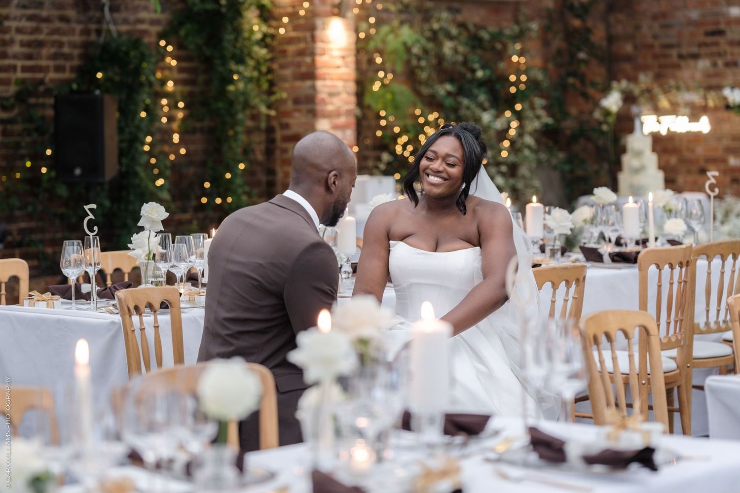 A couple shares a tender moment at their wedding reception surrounded by elegant table settings and twinkling lights.