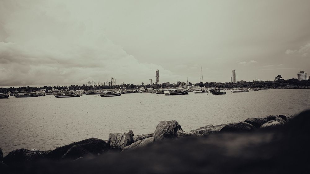 Moody waterfront panorama with distant boats and shoreline silhouetted against a grey sky.