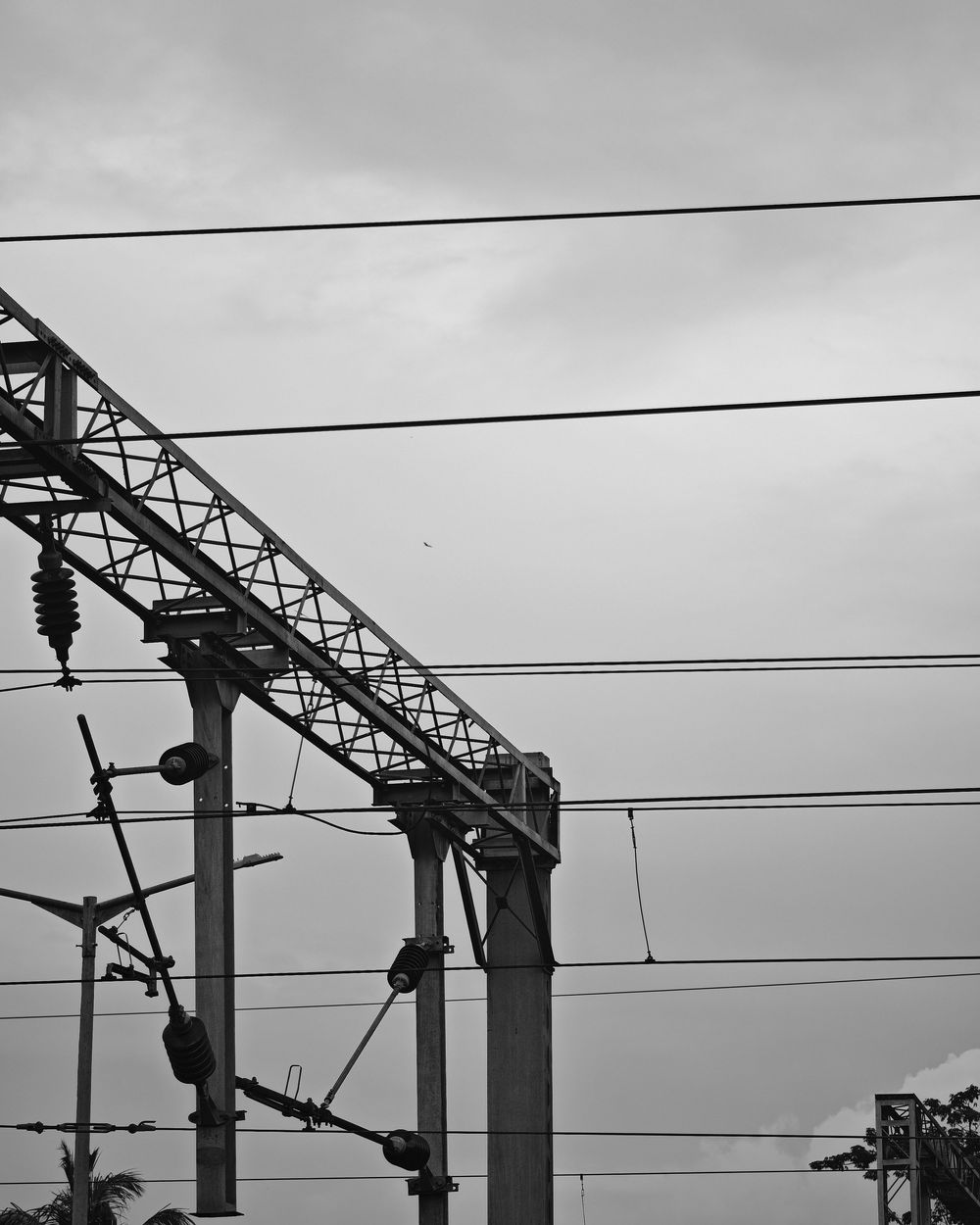 A series of electrical power line poles and transmission towers silhouetted against a cloudy sky in black and white.
