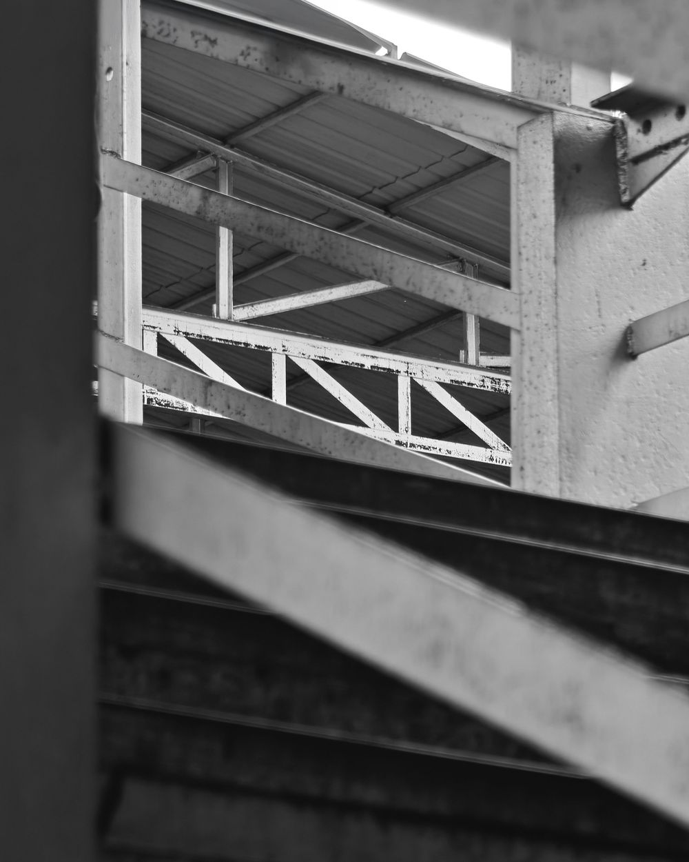 Black and white architectural detail showing metal support beams and structural framework under an angled roof overhang.