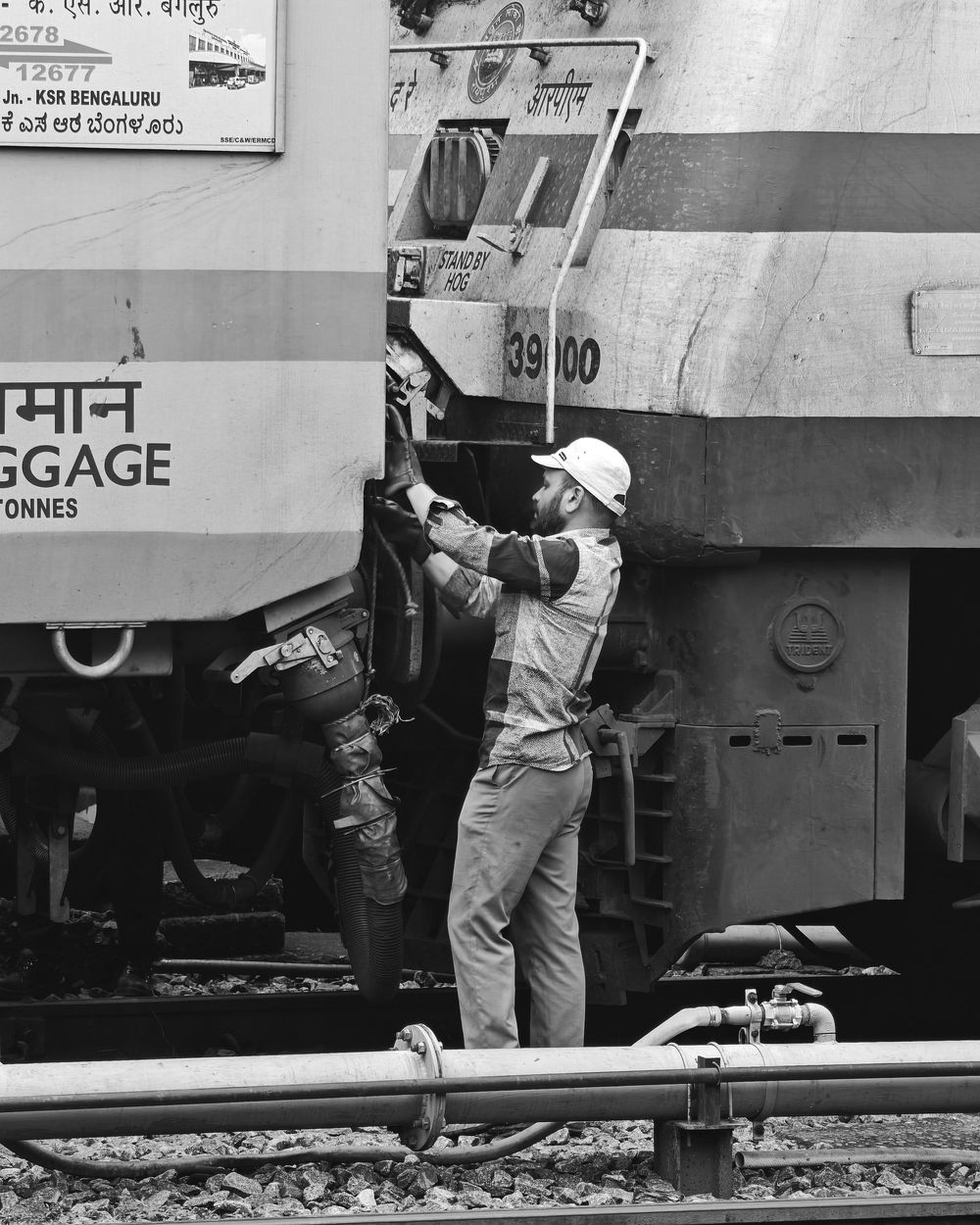 Railway worker in uniform performs maintenance on a train car at a station platform.