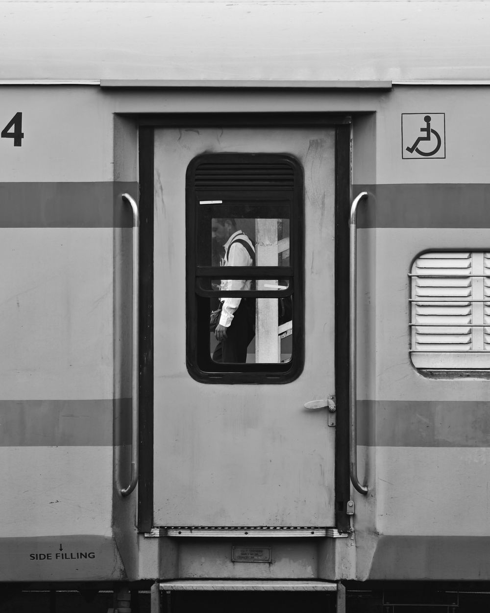 A black and white photograph showing the side of a train car with windows and ventilation panels.