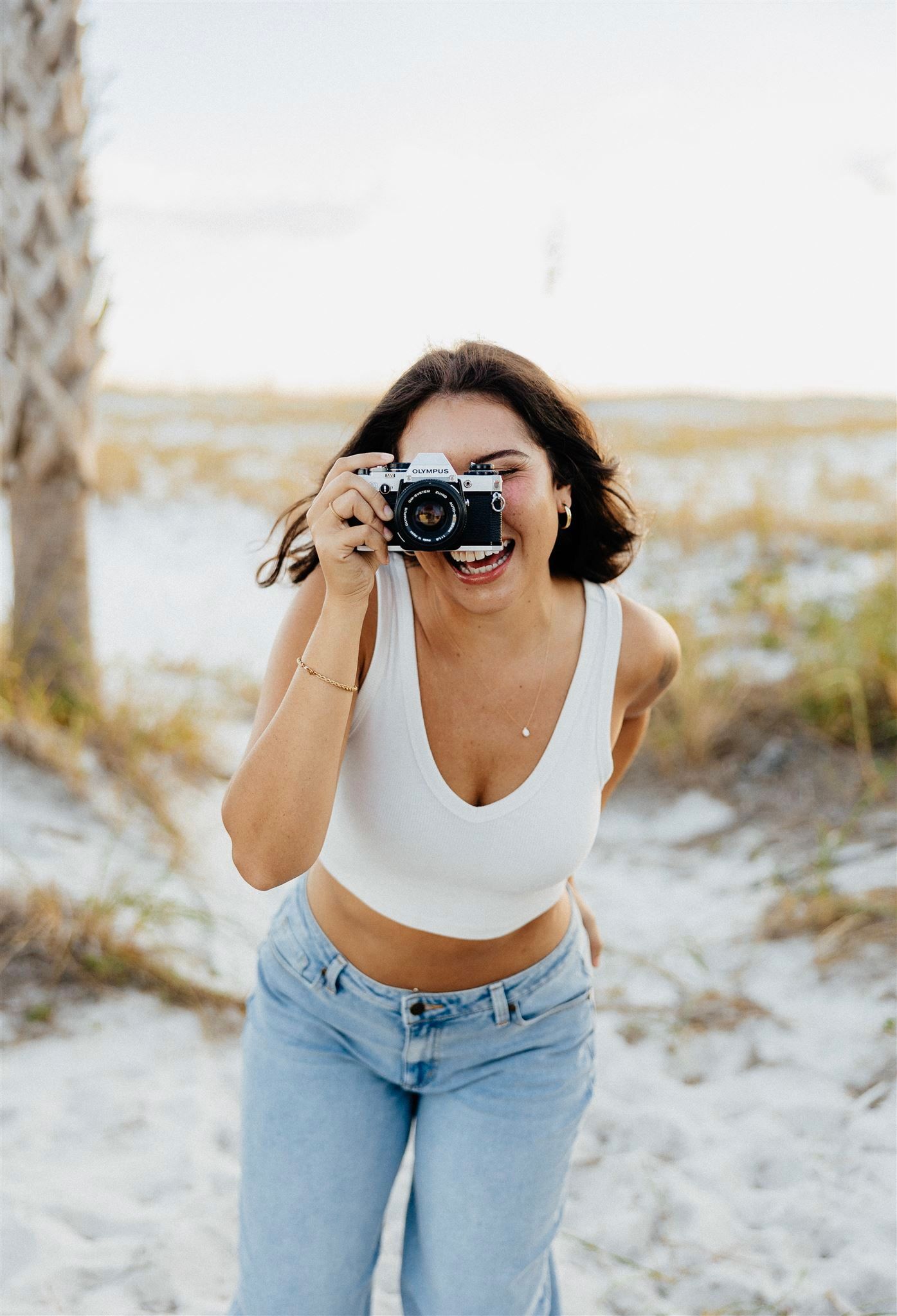 Young photographer in casual attire taking pictures with vintage camera on beach path.