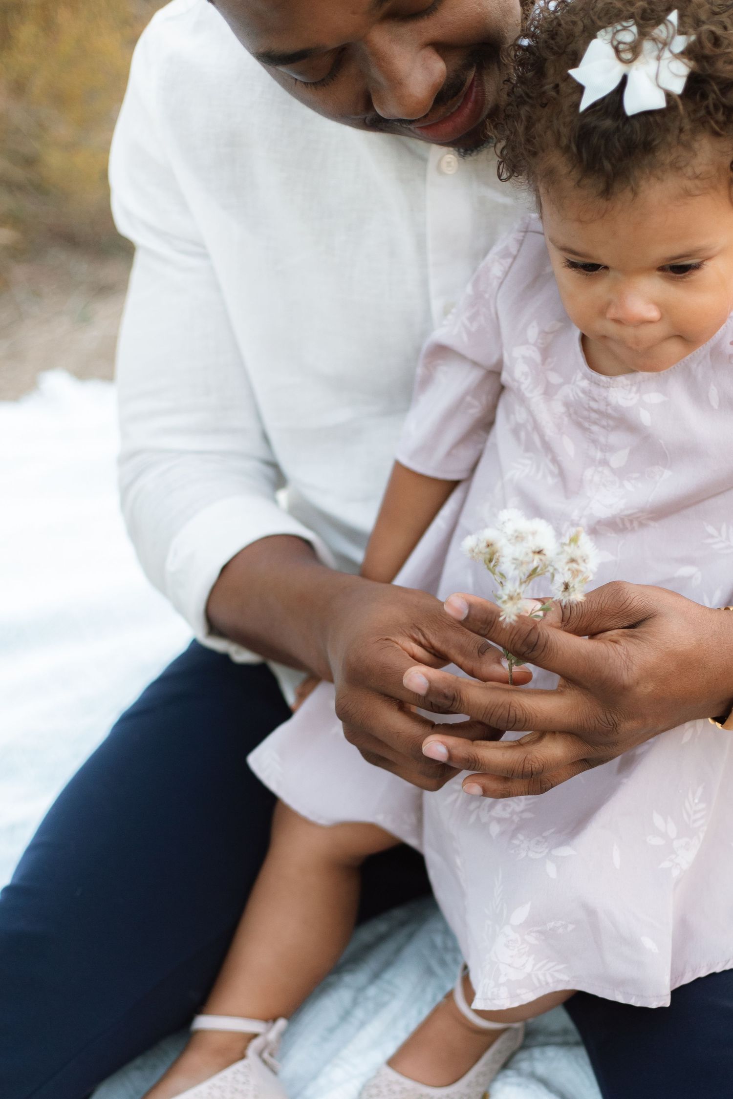 A sweet moment showing hands holding small flowers while sitting together outdoors.