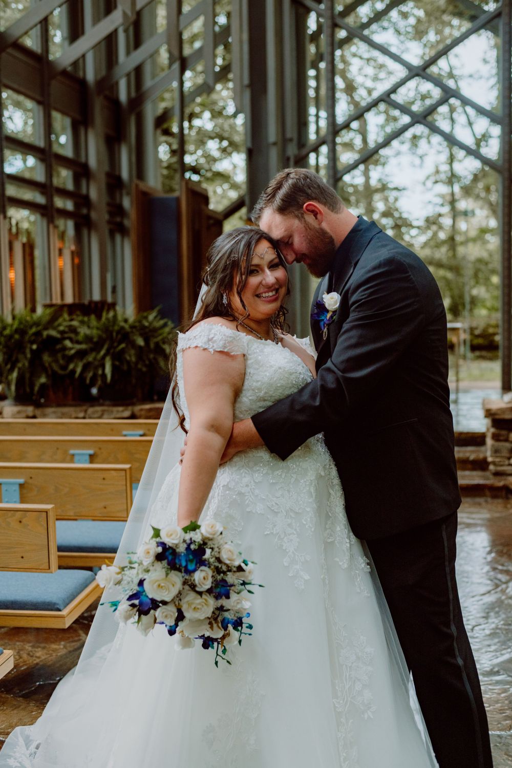 Intimate moment between newlyweds sharing a laugh in a glass-walled chapel.