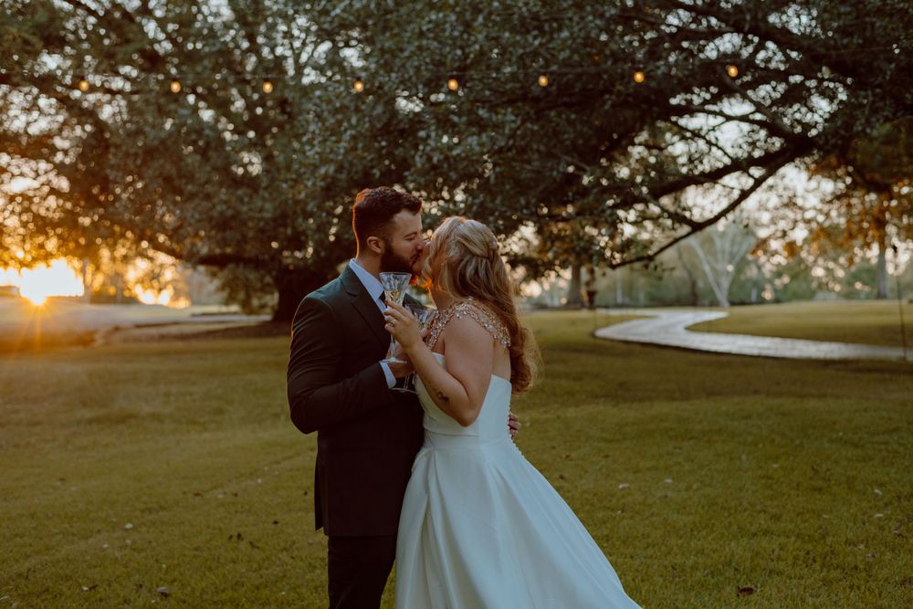 Golden sunset wedding photo of newlyweds embracing on a lush lawn.