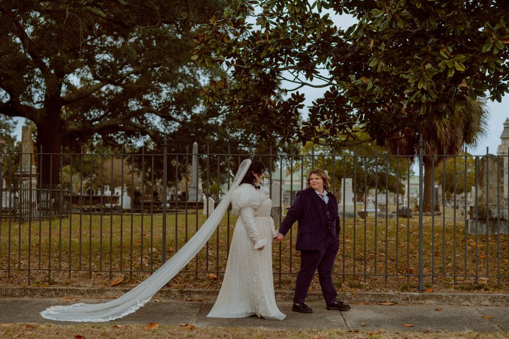 A couple poses near an iron cemetery fence with a flowing white wedding veil.