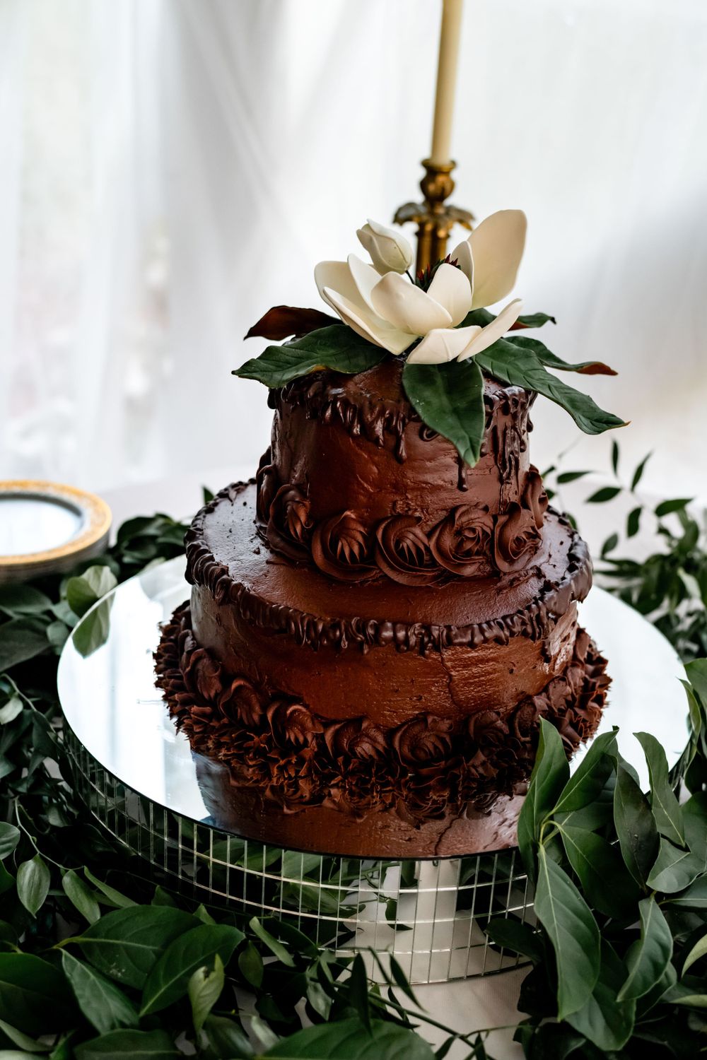 Three-tiered chocolate wedding cake decorated with white magnolia and greenery.
