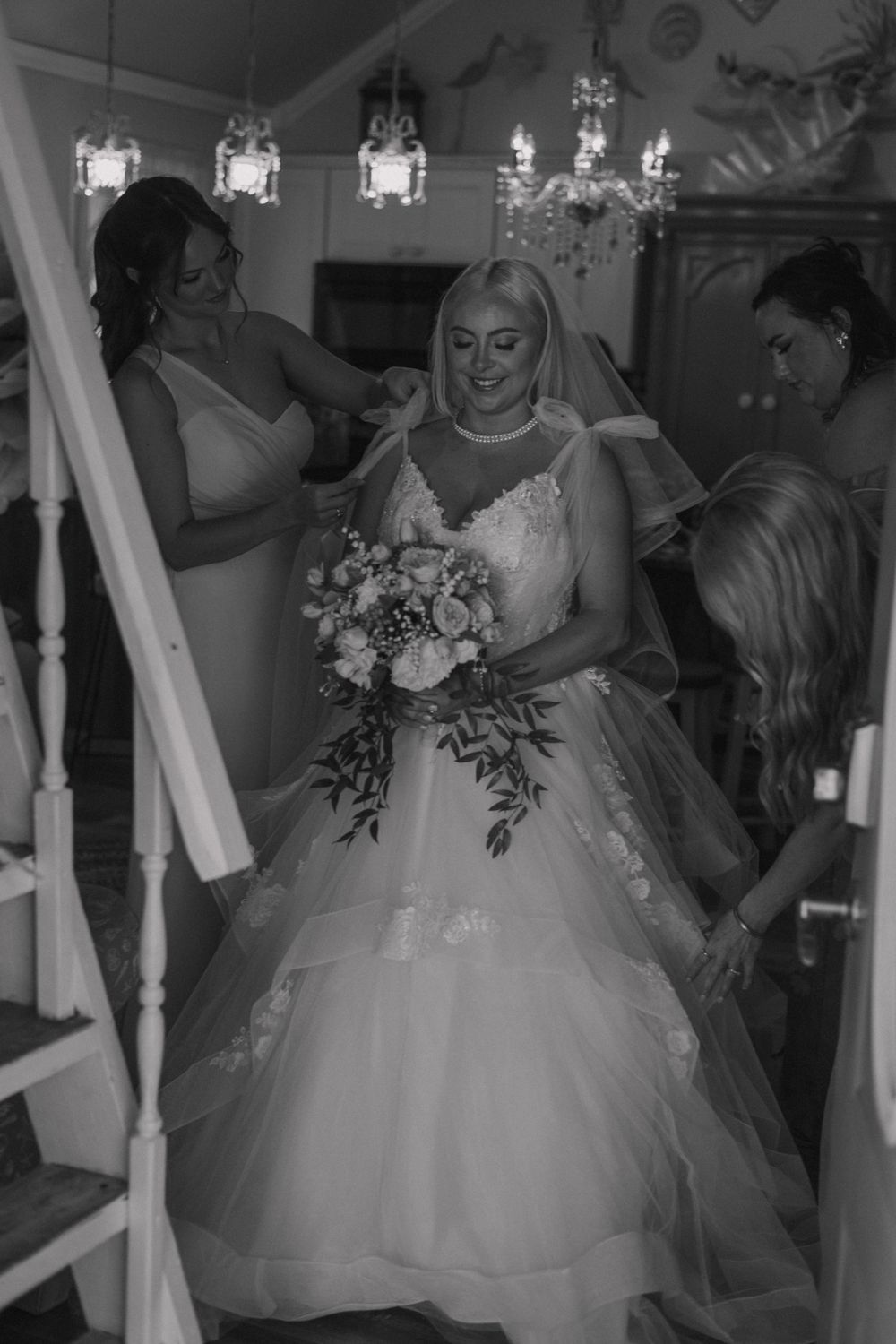 Black and white portrait of bride getting ready with wedding party under chandelier lighting.