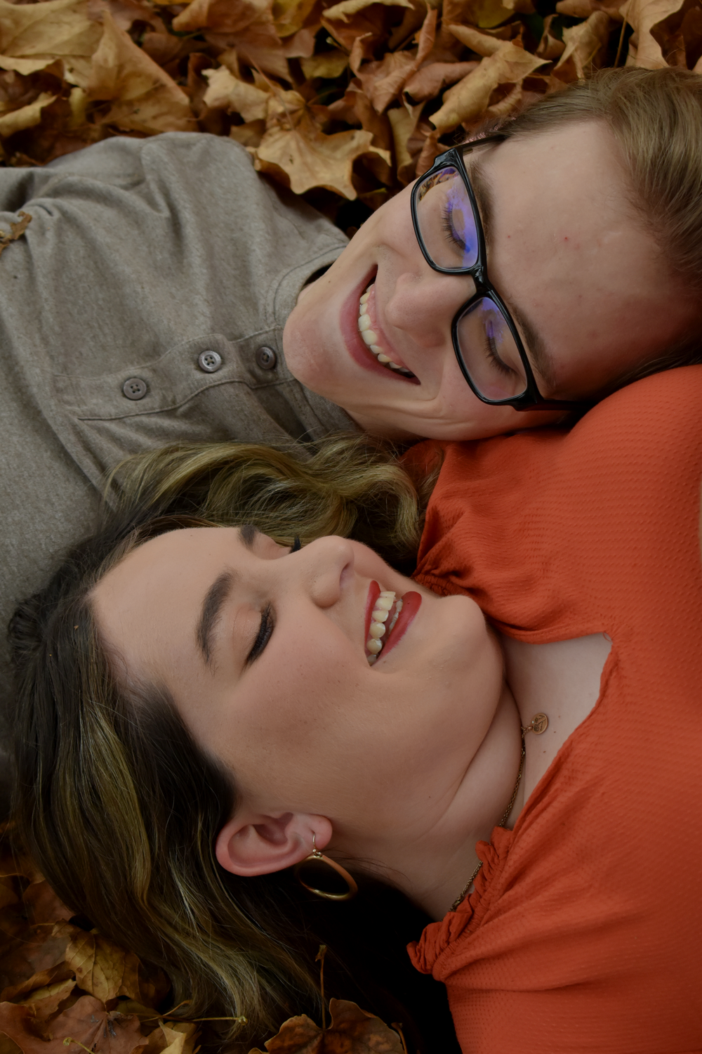 Two people lay in autumn leaves sharing joyful laughter.
