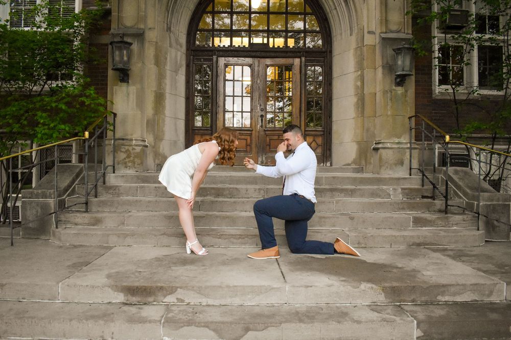 A romantic proposal moment captured at an ornate stone entrance with gothic architecture on the steps of a building.