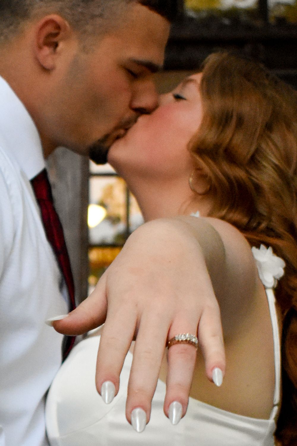 A close-up wedding photo showing a tender kiss, with the bride's hand displaying an elegant engagement ring and white manicure.