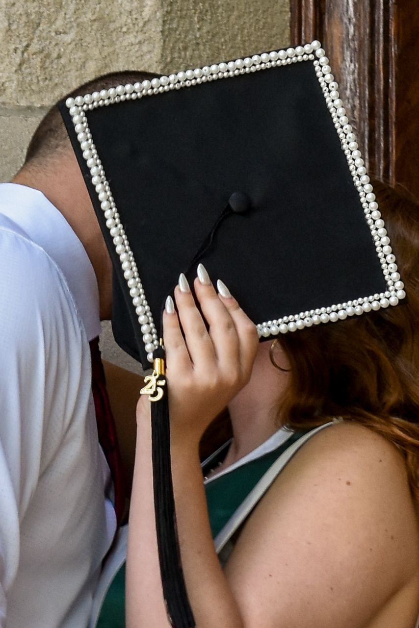 A graduation cap decorated with rhinestones around the border being held up during a special moment.