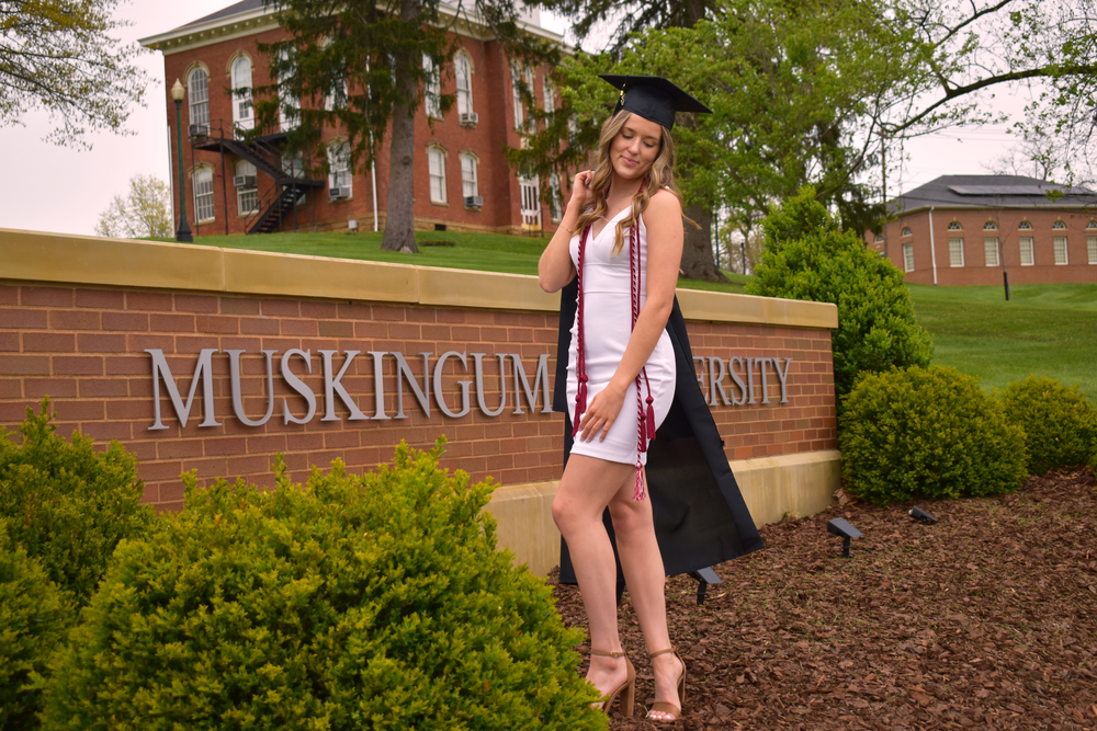 A graduation photo showcasing the Muskingum University entrance sign with brick buildings in the background.