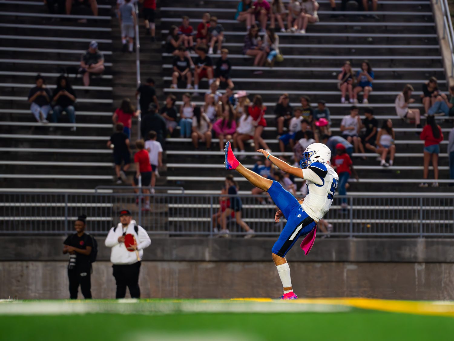 Football punter executing high kick during night game with crowd in background.