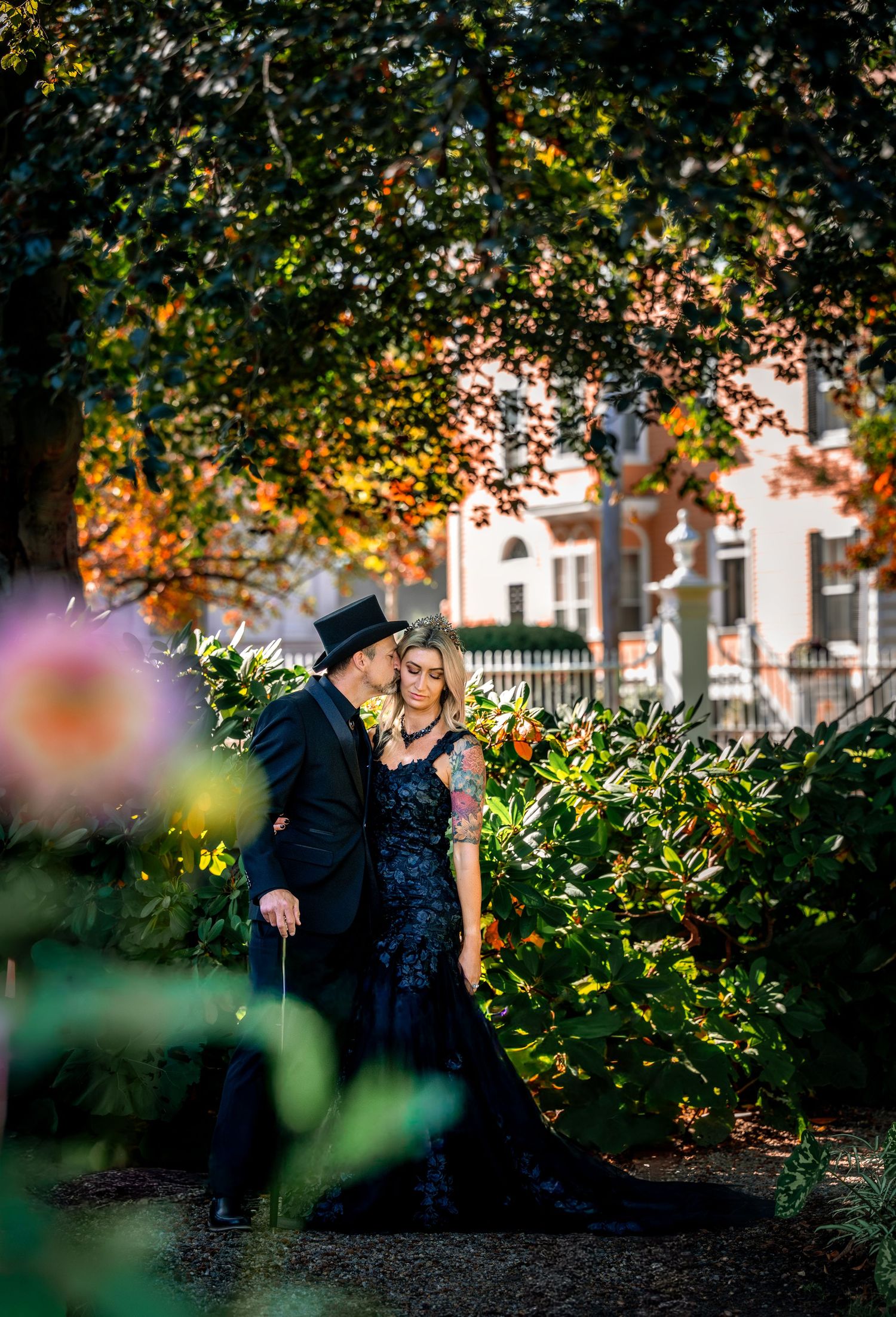 A woman in black stands near a white picket fence in front of a traditional colonial house.