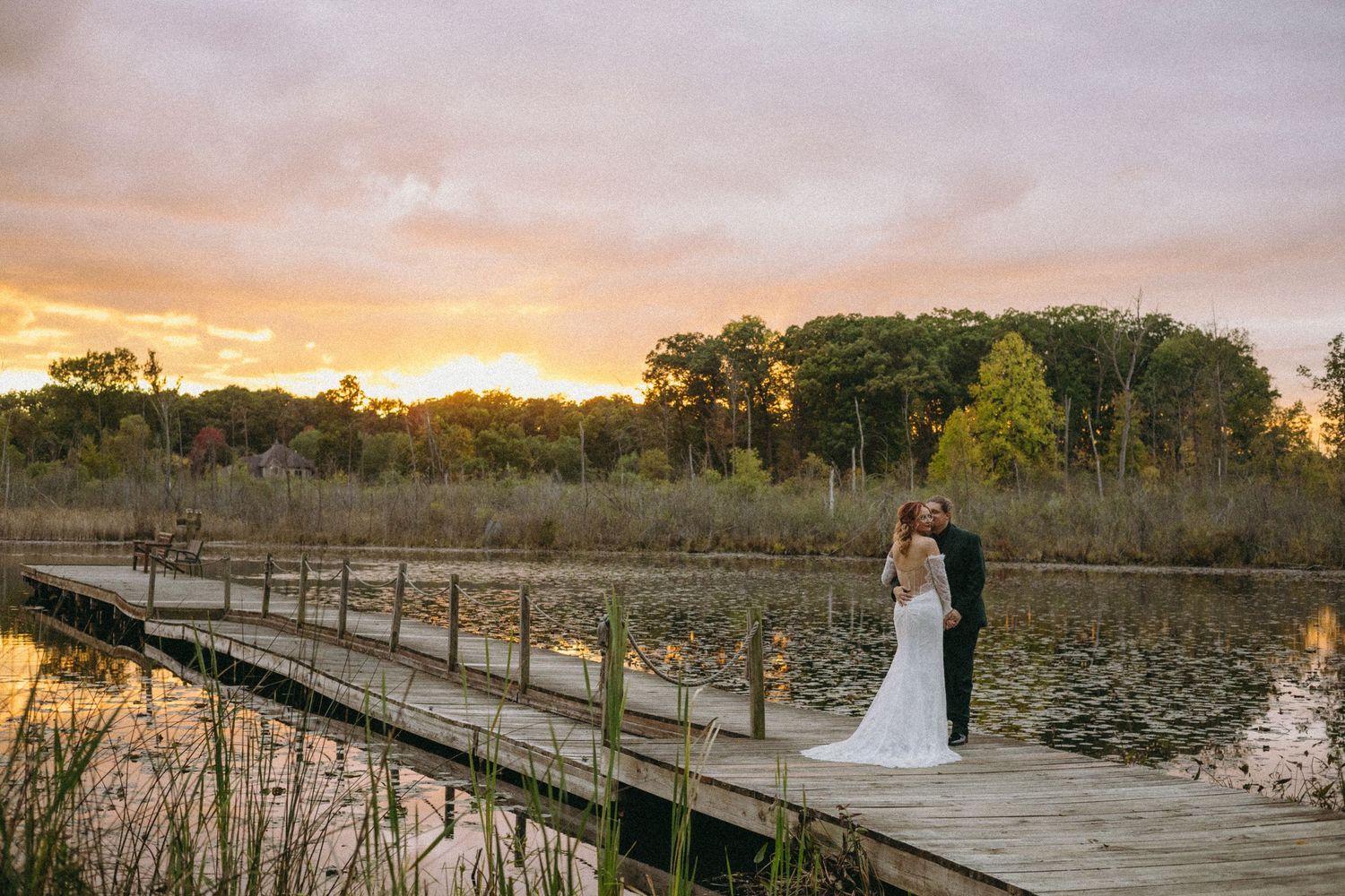 A bride and groom share an intimate, candid moment on the dock overlooking a beautiful and vibrant sunset in Ann Arbor, Michigan.